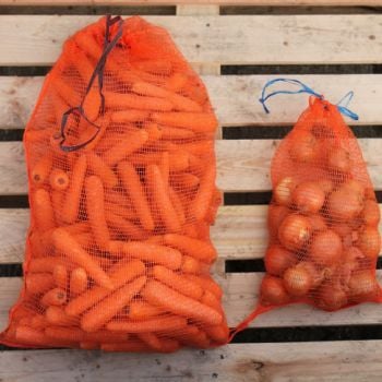 Two orange vegetable nets filled with carrots and onions, tied at the top, resting on a wooden surface.
