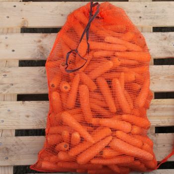 Orange vegetable nets filled with carrots, tied at the top, resting on a wooden surface.