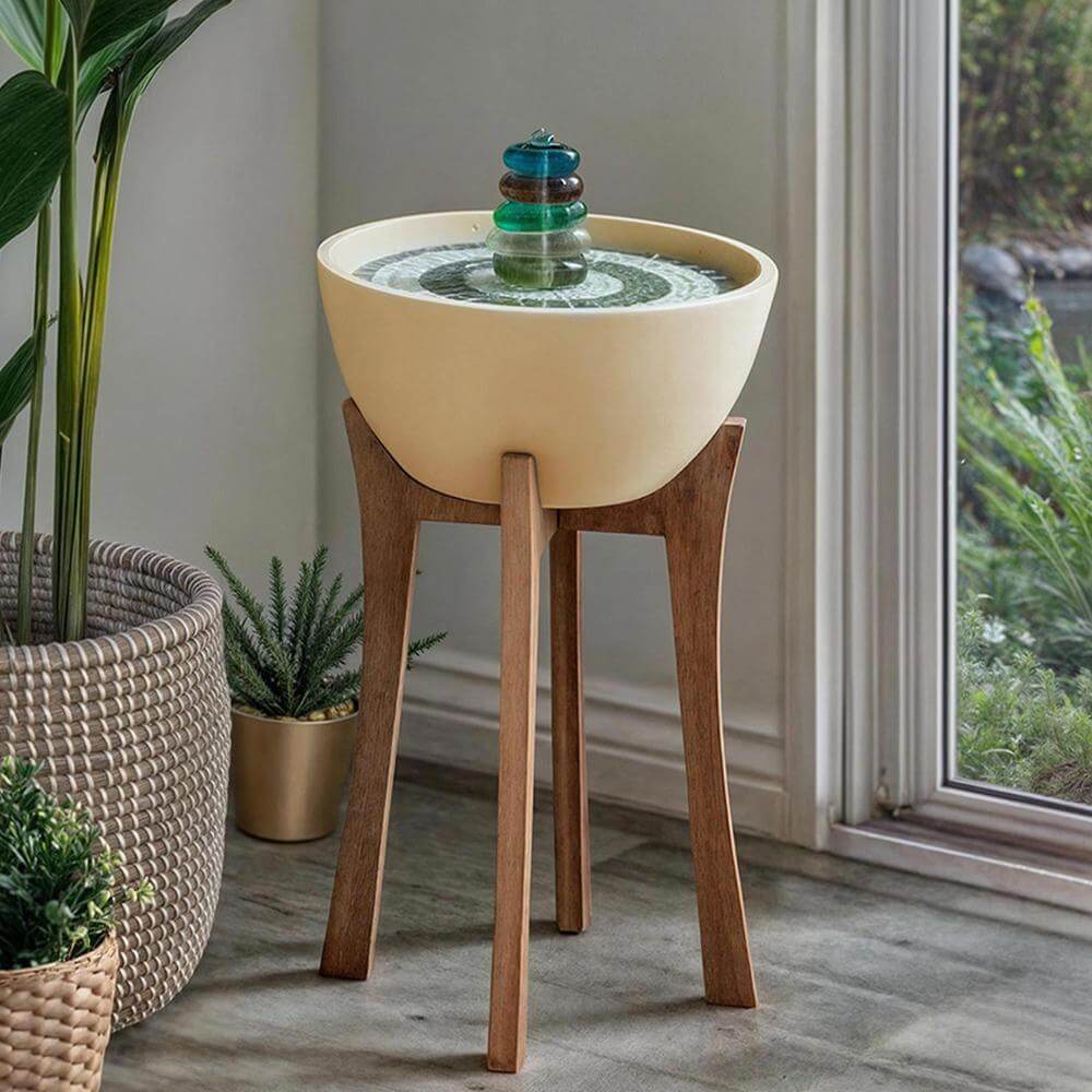 Small indoor fountain on a wooden stand with plants around