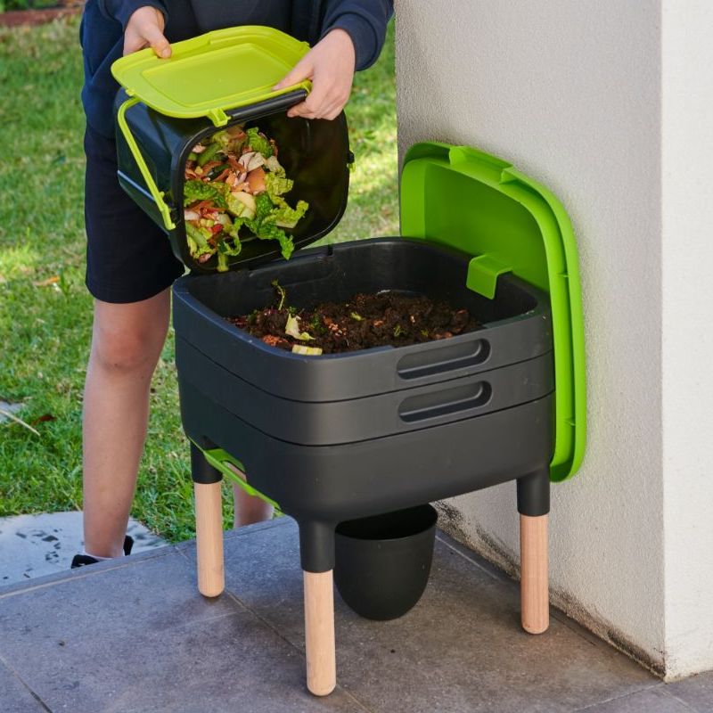 Someone adding kitchen waste to a wormery in garden