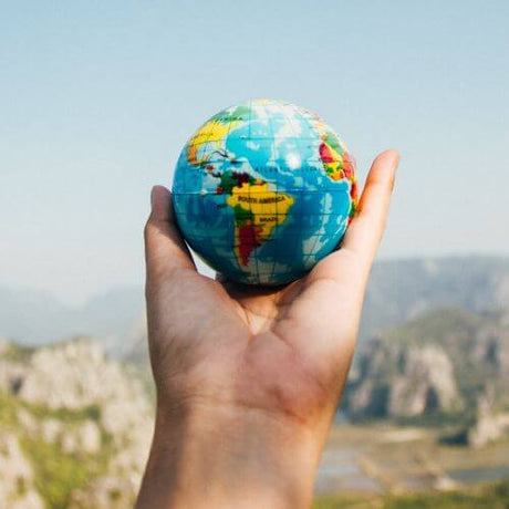 A Hand holding a toy world with mountains in background