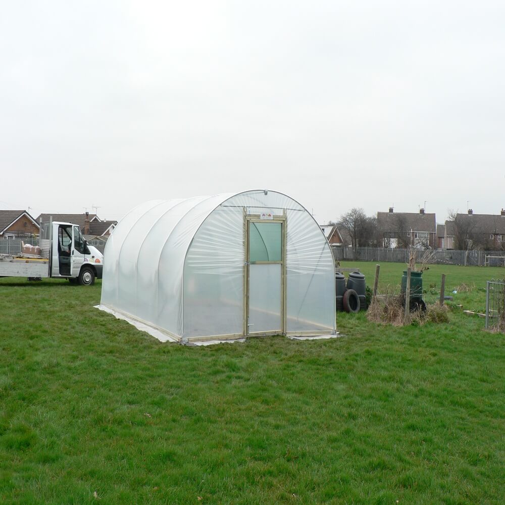 Polycarbonate greenhouse on a grassy field with a truck in the background