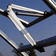 Close-up of a metal roof truss frame with aluminum beams, black brackets, and a blue sky background.