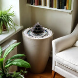 Hydria fountain in a plant pot in the corner by a chair