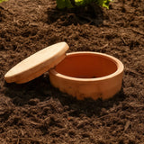 Terracotta pot with lid on a soil background