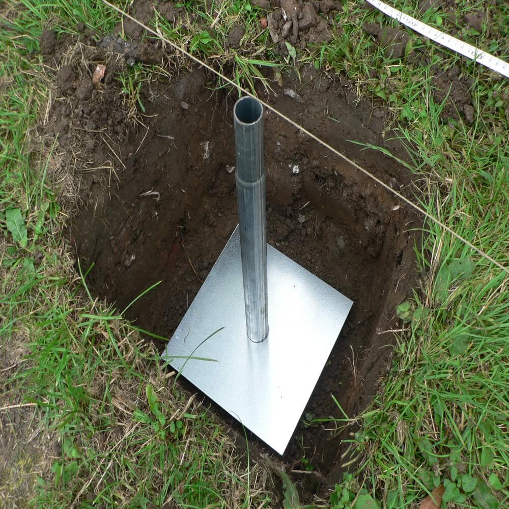 Metal pipe and base in a dug hole on grass