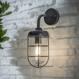 Black barn light hanging on brick wall with light on