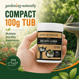 A hand holding a white tub of garden-ng-naturally Compact 100g Bird Bath Cleaner against a blurred garden background with a birdbird and birdbasin.