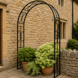 Decorative metal arch with potted plants against a stone building.