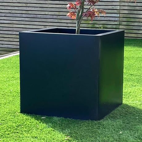 Black cube plant pot in garden with fence in background
