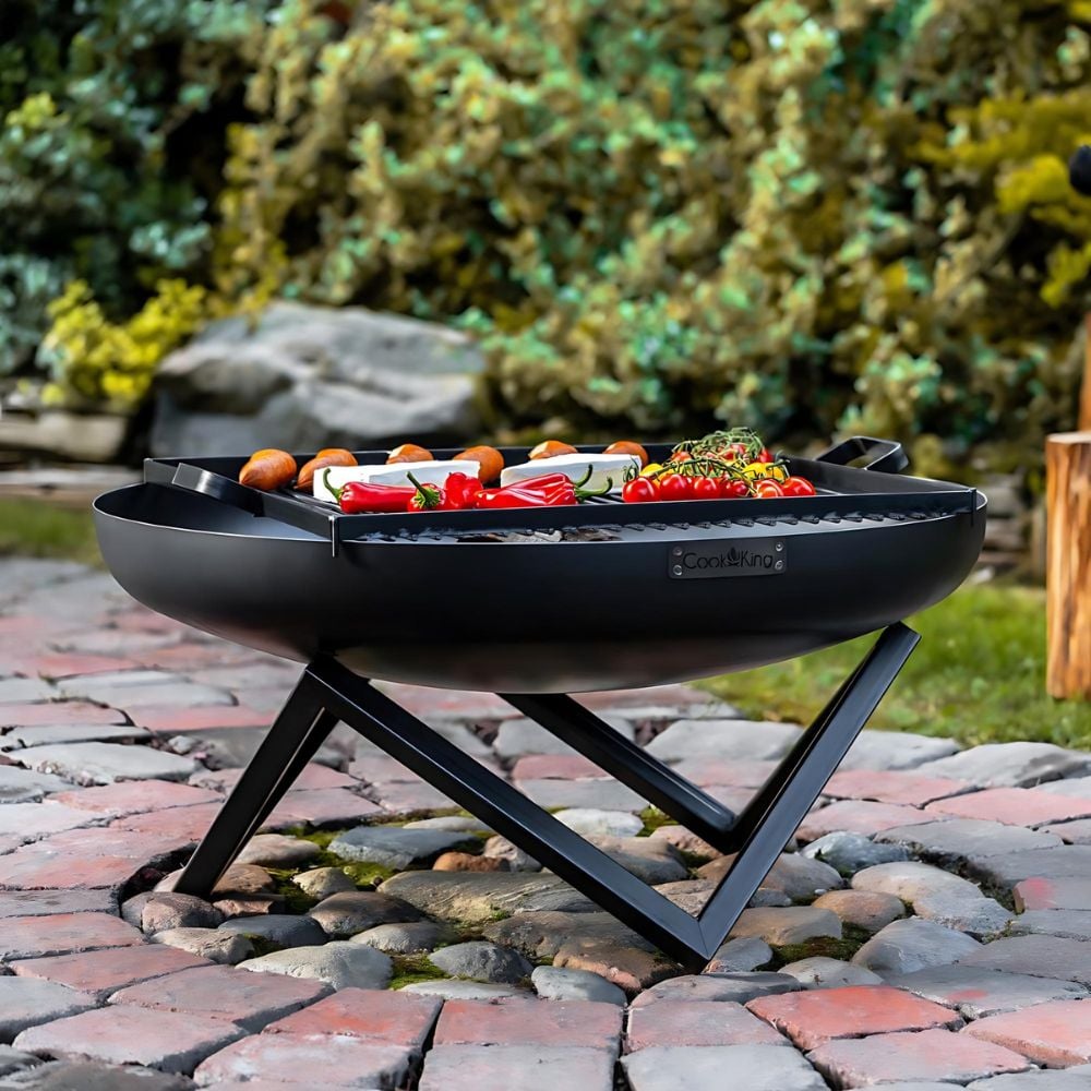A black fire pit with food on grill above on patio.