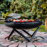 A black fire pit with food on grill above on patio.