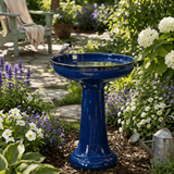 Blue bird bath in a garden with flowers and a chair in the background