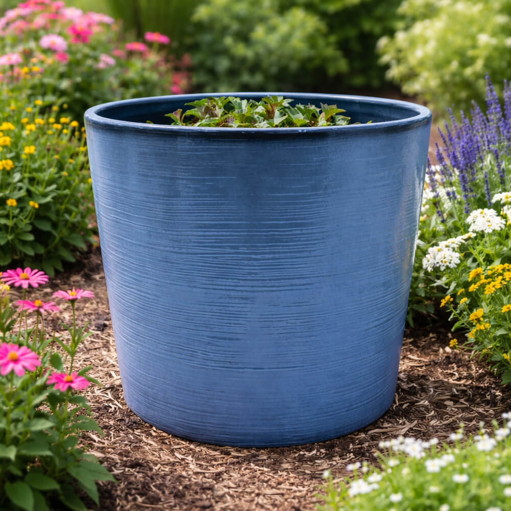 Blue planter with plants in a garden setting with flowers and mulch
