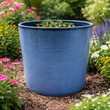 Blue planter with plants in a garden setting with flowers and mulch