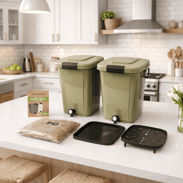 Two green trash bins on a kitchen counter with kitchen items in the background.
