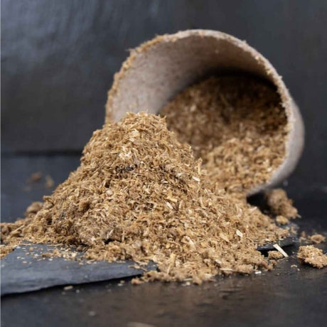 coarse brown bokashi bran pile in front of a seedling pot