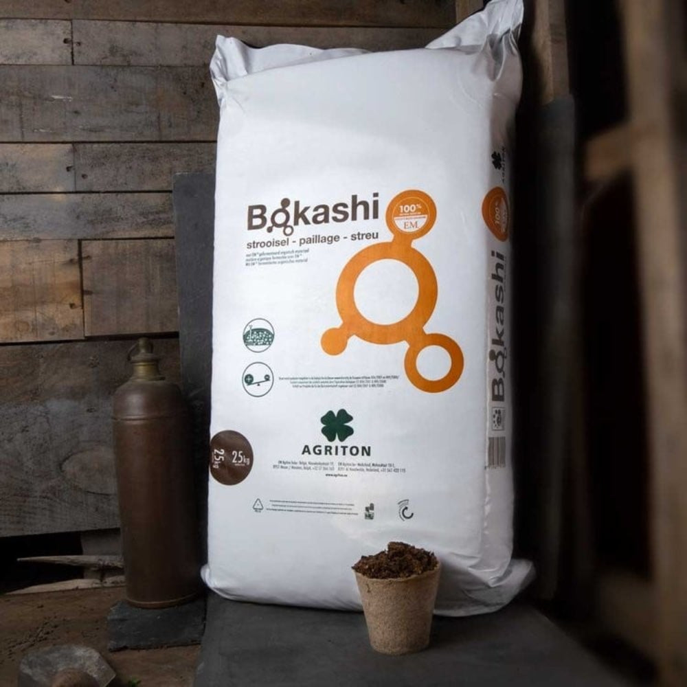 white bag filled with bokashi bran stood upright in a shed with a seedling pot in front 