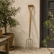 Garden fork leaning against a wall next to a potted plant