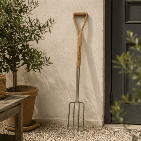 Garden fork leaning against a wall next to a potted plant