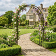 Floral archway in a garden with a stately home in the background
