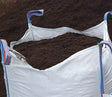 A bulk bag of wool compost for seeds, with a blue and red twine handle and a partially opened top, set against a background of soil.