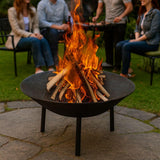 cast iron fire pit burning logs on a garden patio with people gathered around