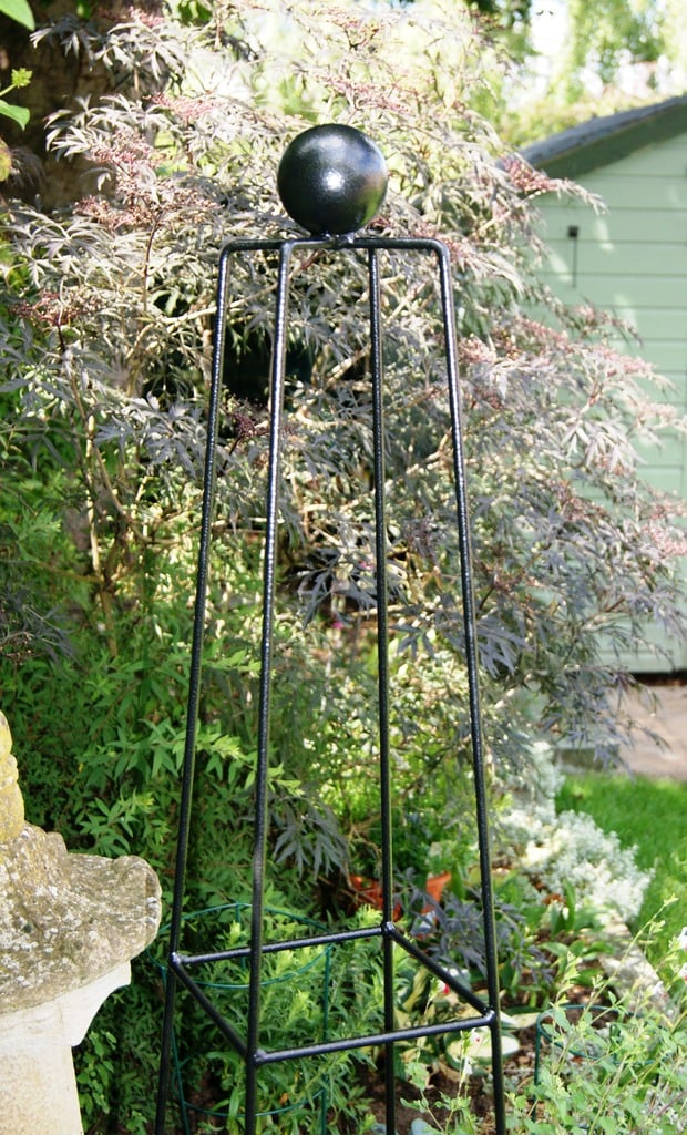 A black metal obelisk garden feature in a garden setting