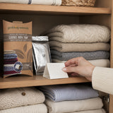 Clothing on a shelf with a hand holding a clothes moth trap packaging.