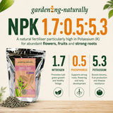 A garden-fertilizer package shown on a light beige background with decorative leaves and text. The product is a silver pouch labeled 'gardenng-naturally' and 'Complex Fertilisers,' with loose dark pellets scattered at the bottom left.