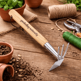 Dual head garden hoe with wooden handle and stainless steel blade and prongs on a potting table for weeding and soil cultivation