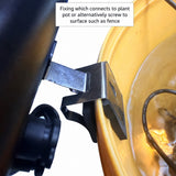 Close-up of a black metal mounting bracket attached to a yellow plastic planter pot, with a text box explaining how the fixture connects to a plant pot or fence.