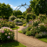 Metal garden archway in a lush garden with flowers and trees