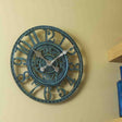 A verdigris mechanical wall clock with Roman numerals, mounted on a wall.