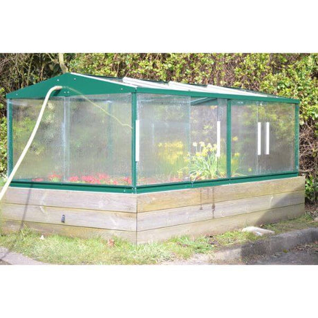 A garden cold frame made of aluminum with reinforced safety glass, containing various plants and vegetables. 