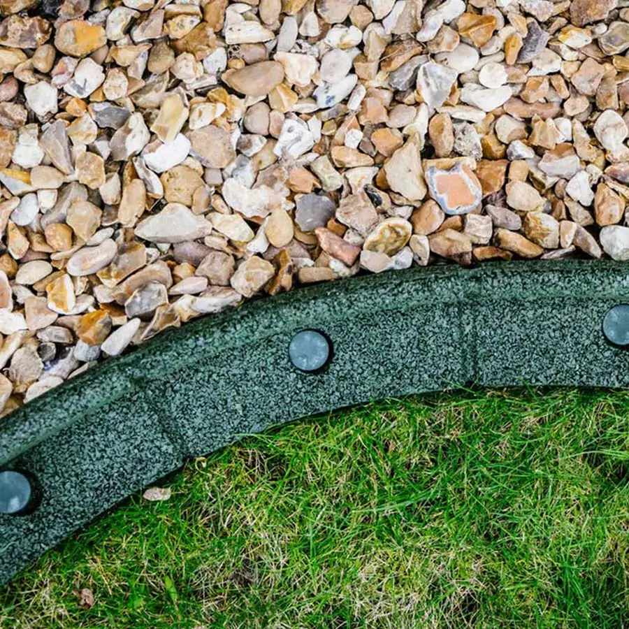 A close-up view of a brown Flexiborder lawn edging panel placed on a grass edge, with a few inches of the panel above the grass surface.