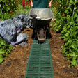 A person laying out green garden track panels in a garden setting to create a pathway.