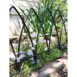 A black, gothic arch garden border edging installed around a flowerbed with green plants and purple flowers.