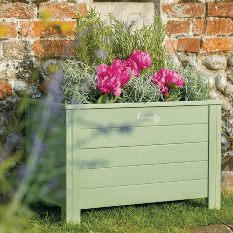 Green wooden trough planter in garden against a wall full of plants