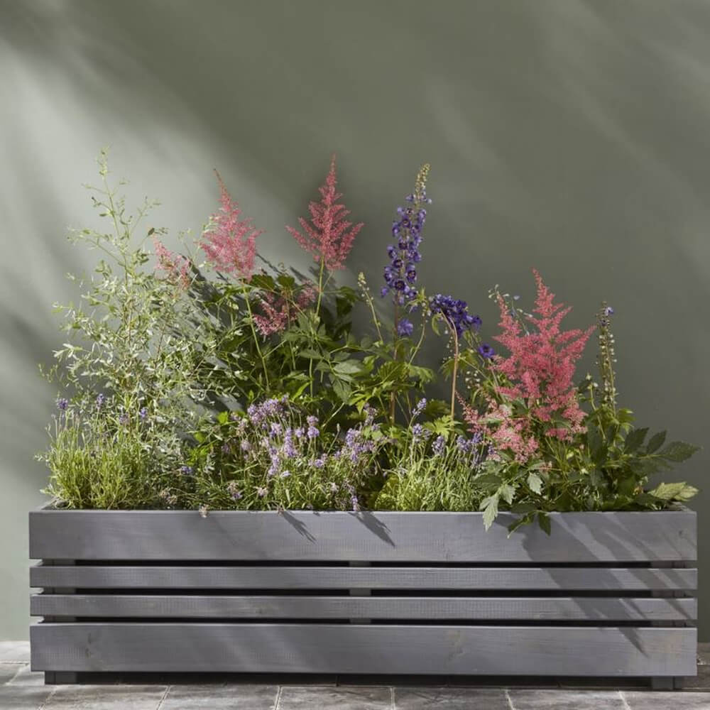 Gray wooden planter with a variety of colorful flower against a gray background