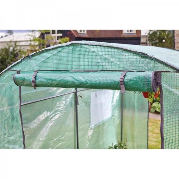 Small greenhouse covered in green plastic, showing door rolled up
