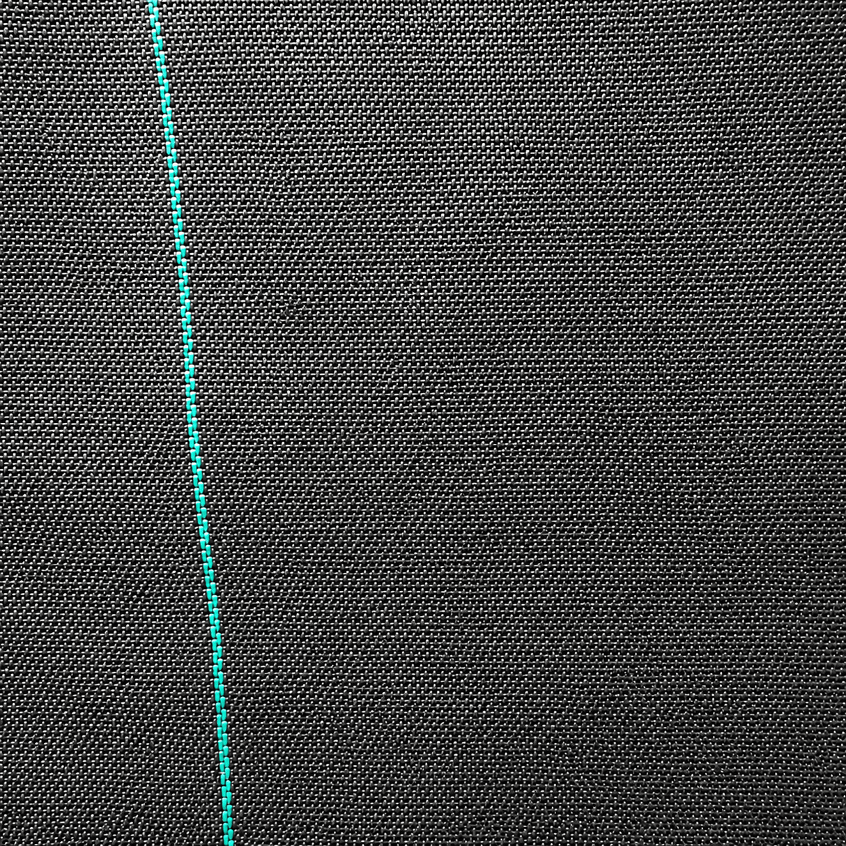 Close-up of black fabric with a green thread running vertically