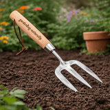 Hand garden fork with wooden handle and stainless steel tines breaking up soil in a flower bed for planting and cultivation