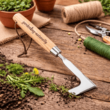 Gardening tool with wooden handle labeled 'Gardening Naturally' on a wooden surface with plants and tools.