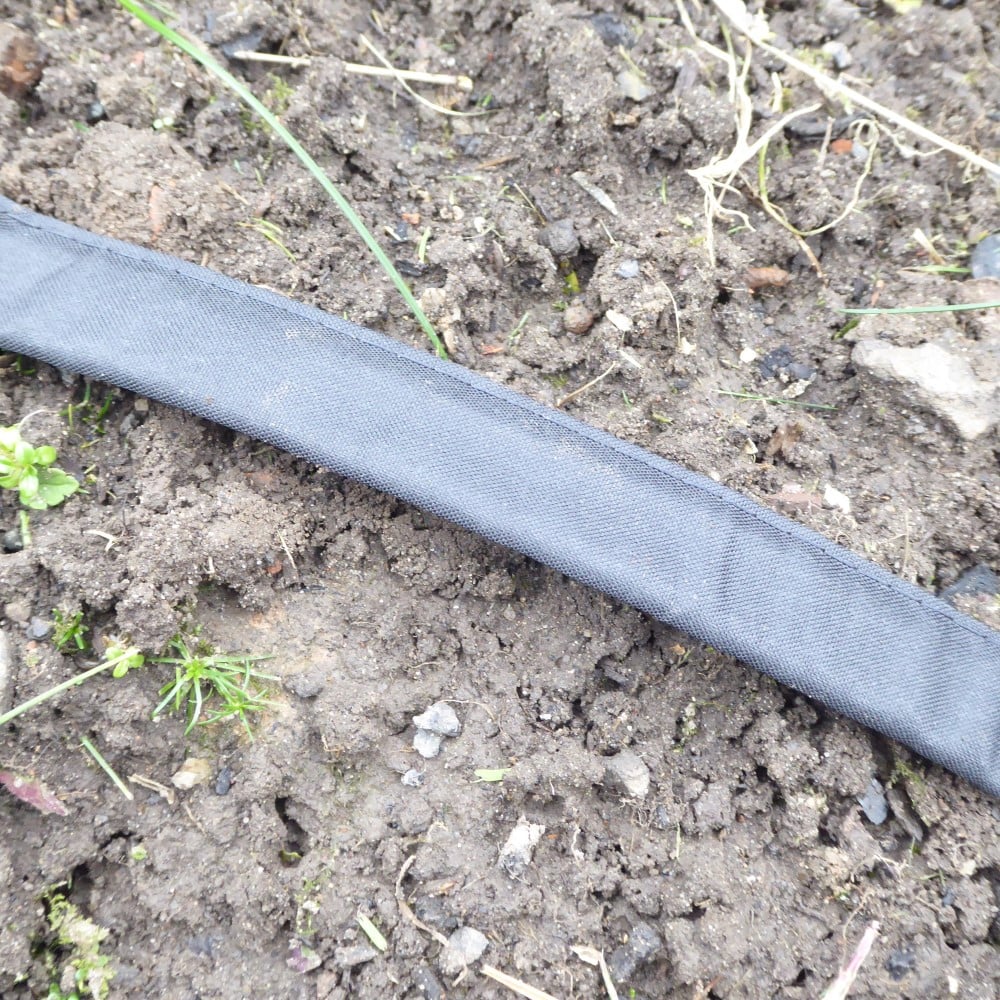 A flat irrigation hose laid on soil with ground securing stakes around it.