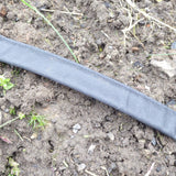 A flat irrigation hose laid on soil with ground securing stakes around it.