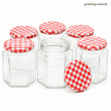 Six clear glass hexagonal jars with red and white gingham patterned lids, arranged on a white background. One jar is open in the center, and one lid is placed in front.