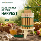 A wooden home juicer with green metal bands and a white mesh strainer sits on a small cream-colored stand on a rustic wooden table. The scene is set in an apple orchard with baskets of apples and pears, a glass pitcher of juice, and text overlays reading 'MAKE THE MOST OF YOUR HARVEST' and 'Home Juice Making'.