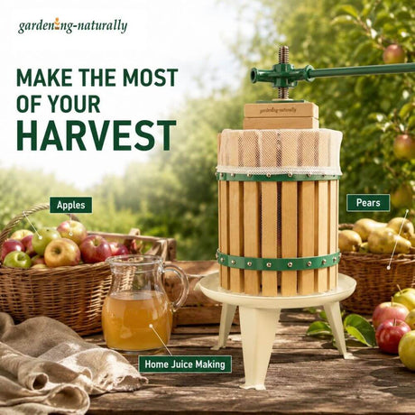 A wooden home juicer with green metal bands and a white mesh strainer sits on a small cream-colored stand on a rustic wooden table. The scene is set in an apple orchard with baskets of apples and pears, a glass pitcher of juice, and text overlays reading 'MAKE THE MOST OF YOUR HARVEST' and 'Home Juice Making'.