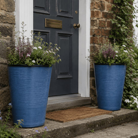 Two blue planters with flowers on either side of a dark gray door.